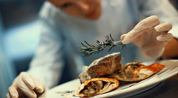 chef placing a sprig of thyme on a dish served on a plate