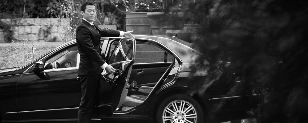 private chauffeur opening the rear door of the car to welcome the customer